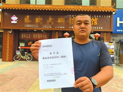 馬先生在自己的營業(yè)房前向記者出示他的購房合同。